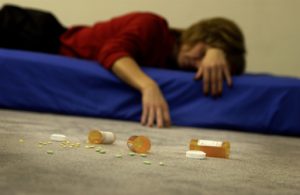 Mid adult woman sprawled on a mattress with vials of pills strewn on the floor