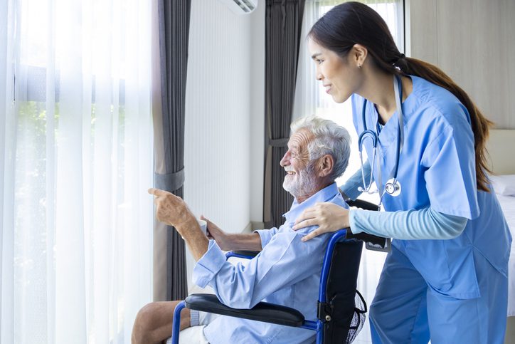 Creating Comforts of Home – Hospice Care at Flushing Hospital Nurse standing behind a wheelchair as a patient points outside the window