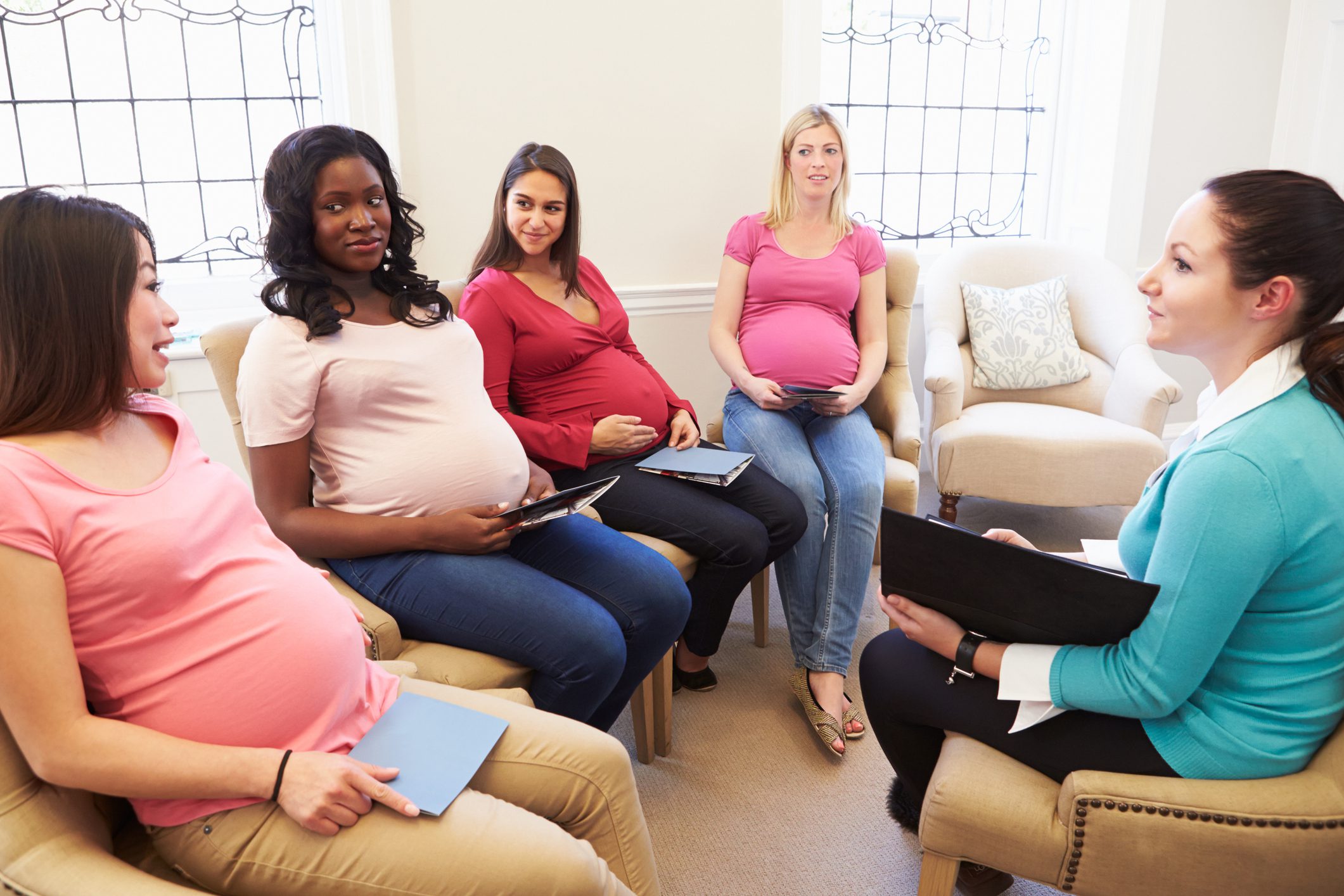 Group of pregnant women with tablets at antenatal class Pregnant Women Smiling In Meeting At Ante Natal Class
